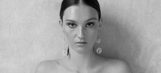 Black and white image of a woman on a textured background with bare shoulders. She is wearing long, dangling pearl earrings from One Dame Lane's bridal collection.